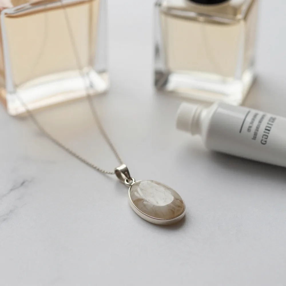 Colgante de piedra natural junto a un perfume y una crema de manos